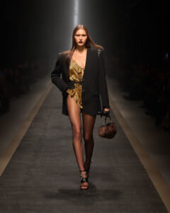 Model walks the runway in an oversized black blazer over a leopard-print dress, carrying a small leopard-print handbag.