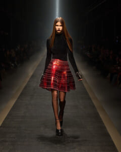 Model walking the runway in a black turtleneck and a red plaid A-line skirt.