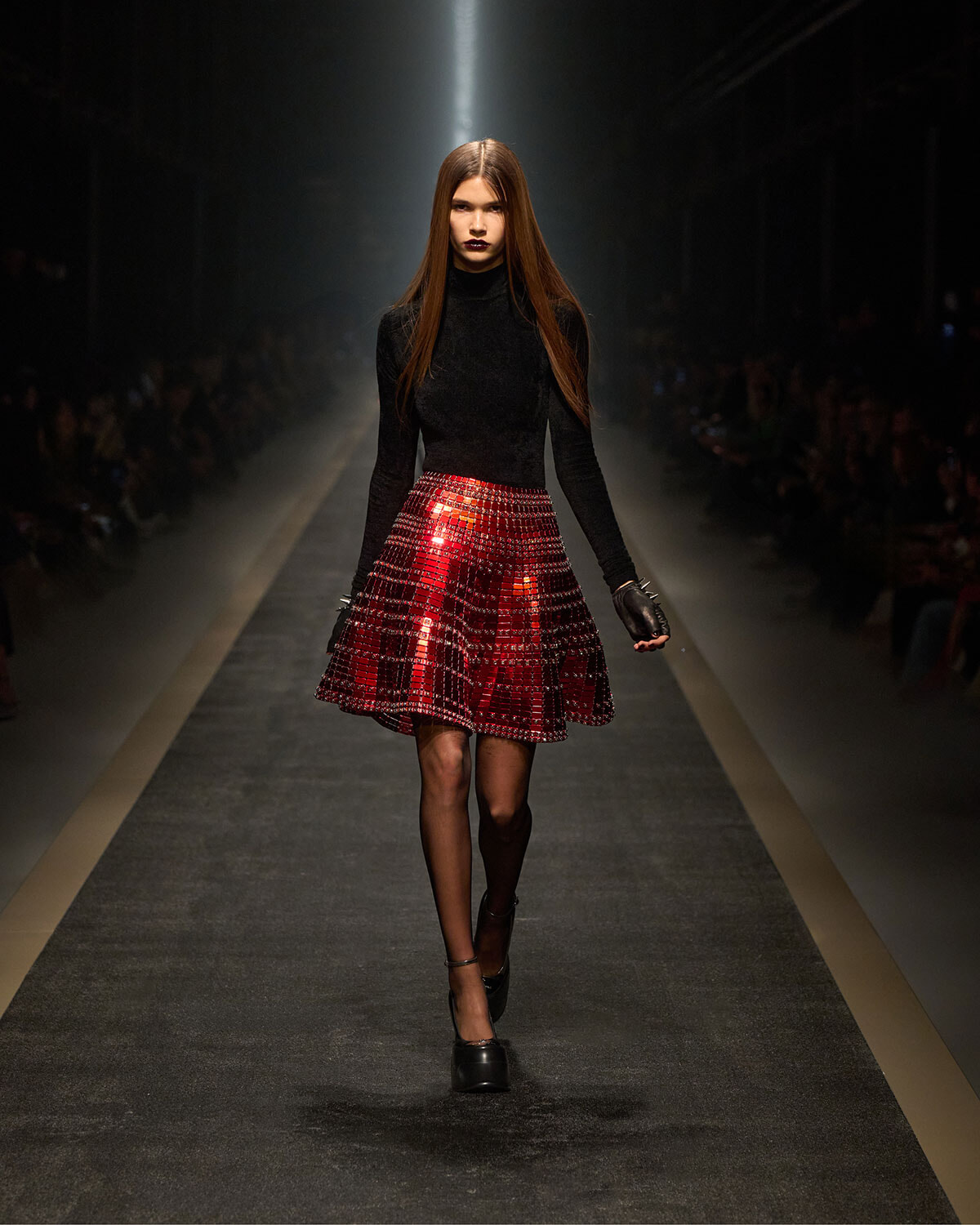 Model walking the runway in a black turtleneck and a red plaid A-line skirt.