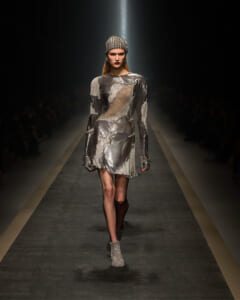 Model walking the fashion runway in a metallic silver dress with a spiked headpiece.