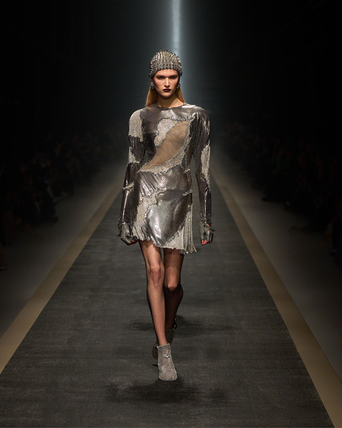 Model walking the fashion runway in a metallic silver dress with a spiked headpiece.