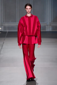 Model walking the runway in a bold pink and red striped knit top with matching wide-leg pants and a relaxed silhouette.