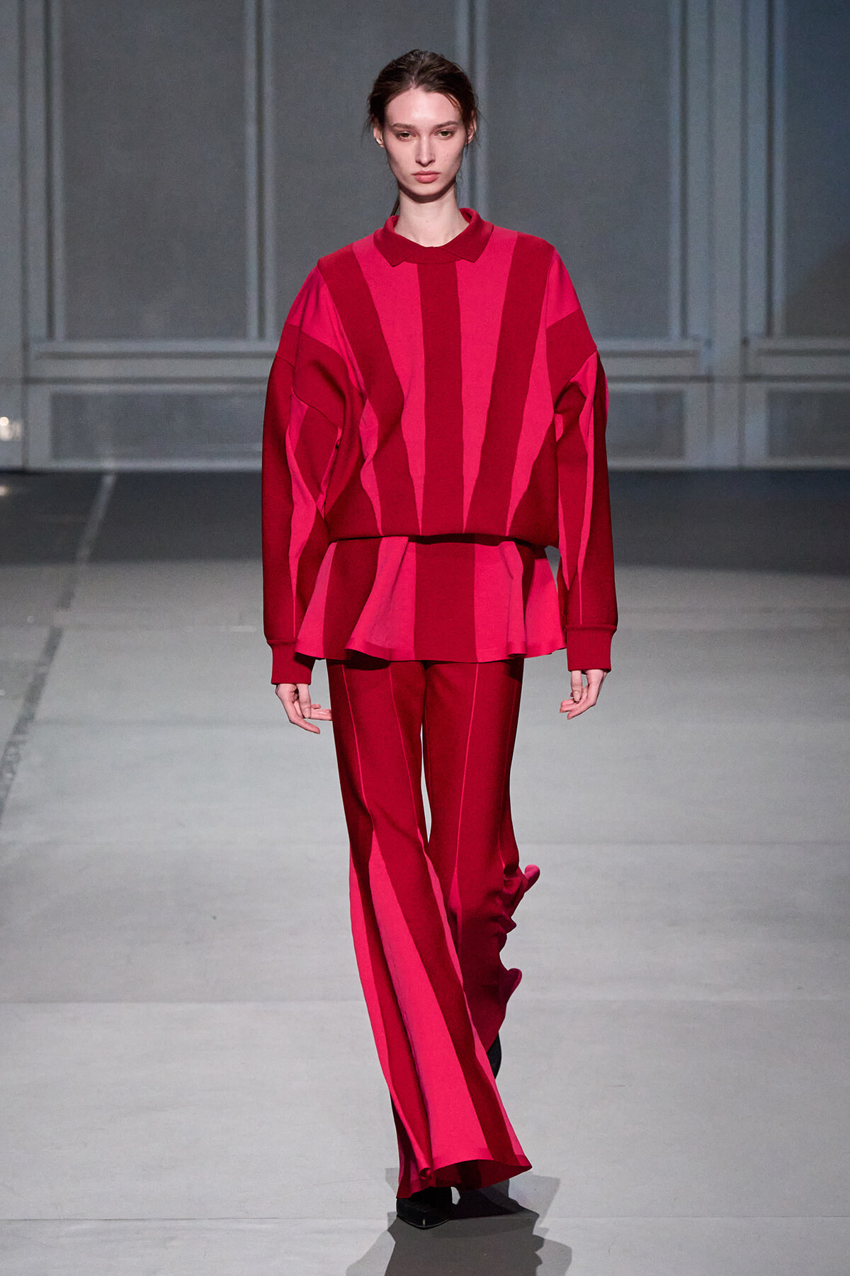 Model walking the runway in a bold pink and red striped knit top with matching wide-leg pants and a relaxed silhouette.