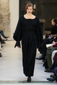 Model walks runway in an all-black, oversized-sleeve outfit with a square neckline and wide trousers.