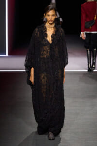 Model walks the runway in a sheer black lace gown and statement choker necklace.