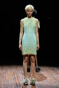 Model on a runway wearing a mint-to-cream sequin dress with a spiked halo headpiece.