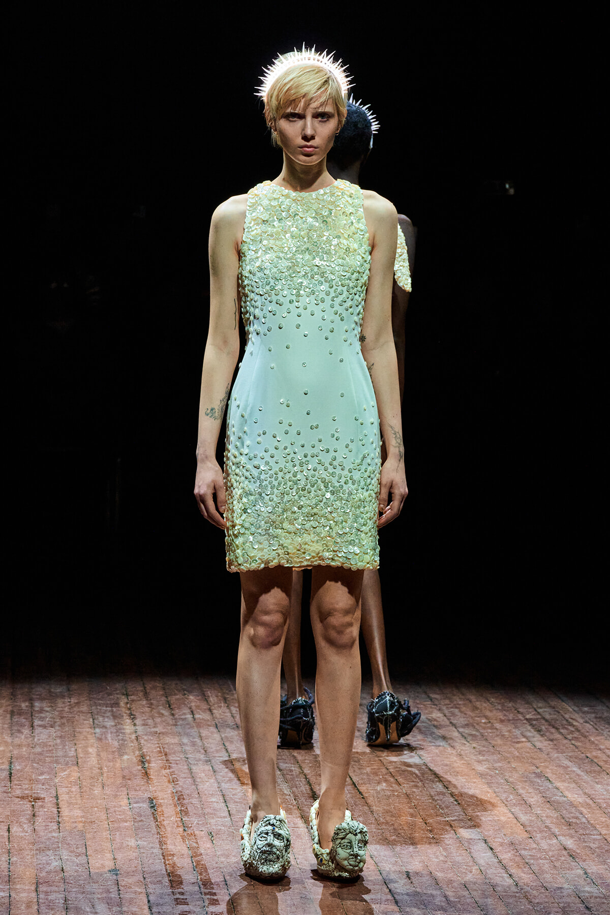 Model on a runway wearing a mint-to-cream sequin dress with a spiked halo headpiece.