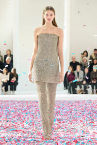 Runway model in a gold beaded strapless jumpsuit walking as colorful confetti falls around her.