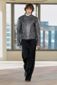 Model wearing a metallic gray textured biker jacket with zip pockets, paired with black wide-leg pants.