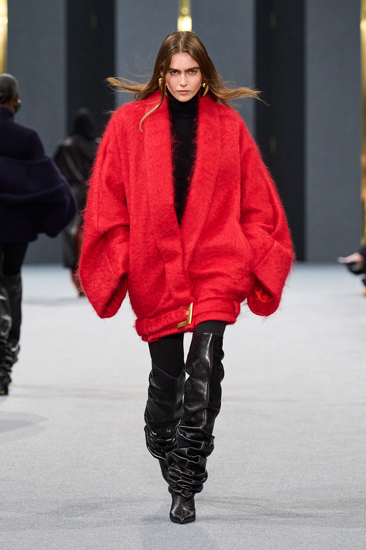 Model walks runway in oversized red fluffy coat over black turtleneck, paired with black ruched knee-high boots.