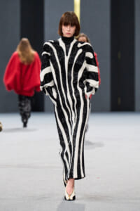 Model walking the runway in a bold black-and-white zebra-stripe knit jumpsuit with voluminous sleeves and a high neckline.