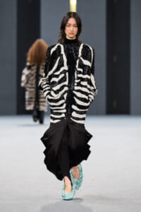 Runway model in a black-and-white zebra-pattern dress with a voluminous black lower skirt and teal shoes.