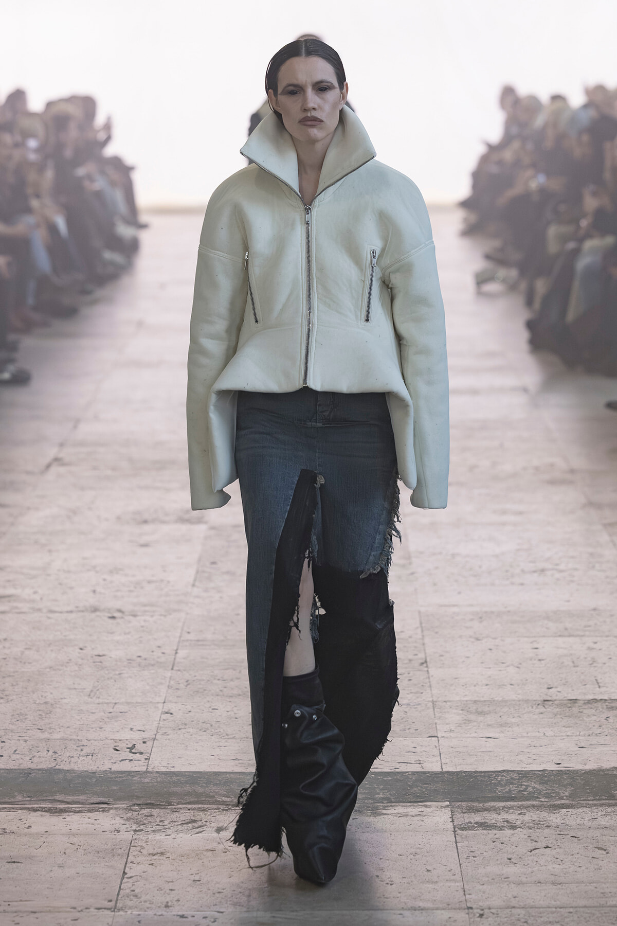 Model walking a runway in a pale mint oversized jacket with a high collar and distressed blue jeans on the catwalk.