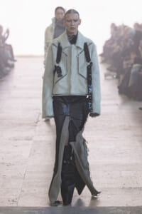 Model walks the runway in a pale blue fur jacket with black utility straps and distressed black pants.