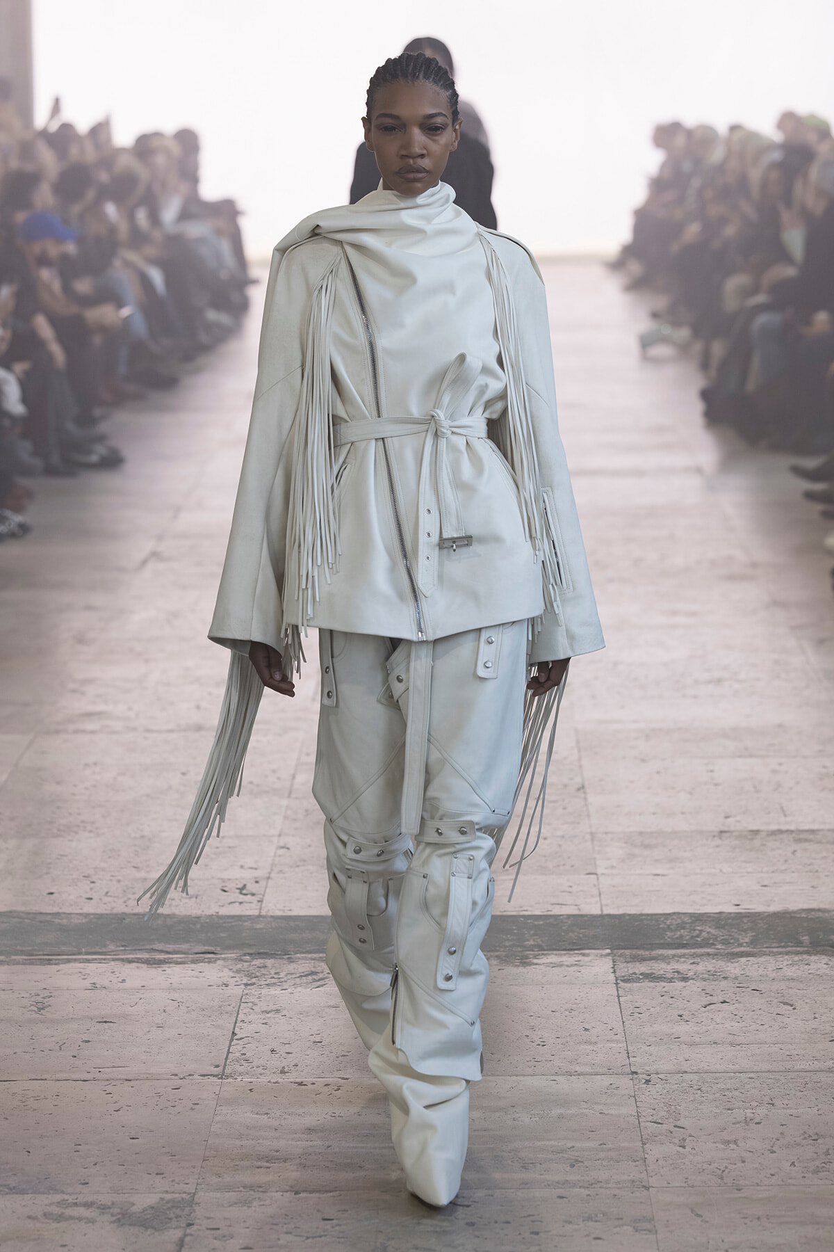 Model walks the runway in an all-white fringe-trimmed coat with a belt and matching utility pants, white boots visible.