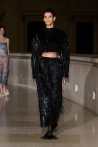 Female model walks a runway in a black, sequined fringe crop top and matching wide-leg pants.