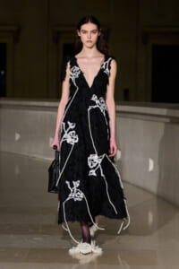 Model in a black sleeveless gown with white floral embroidery walking a runway runway.