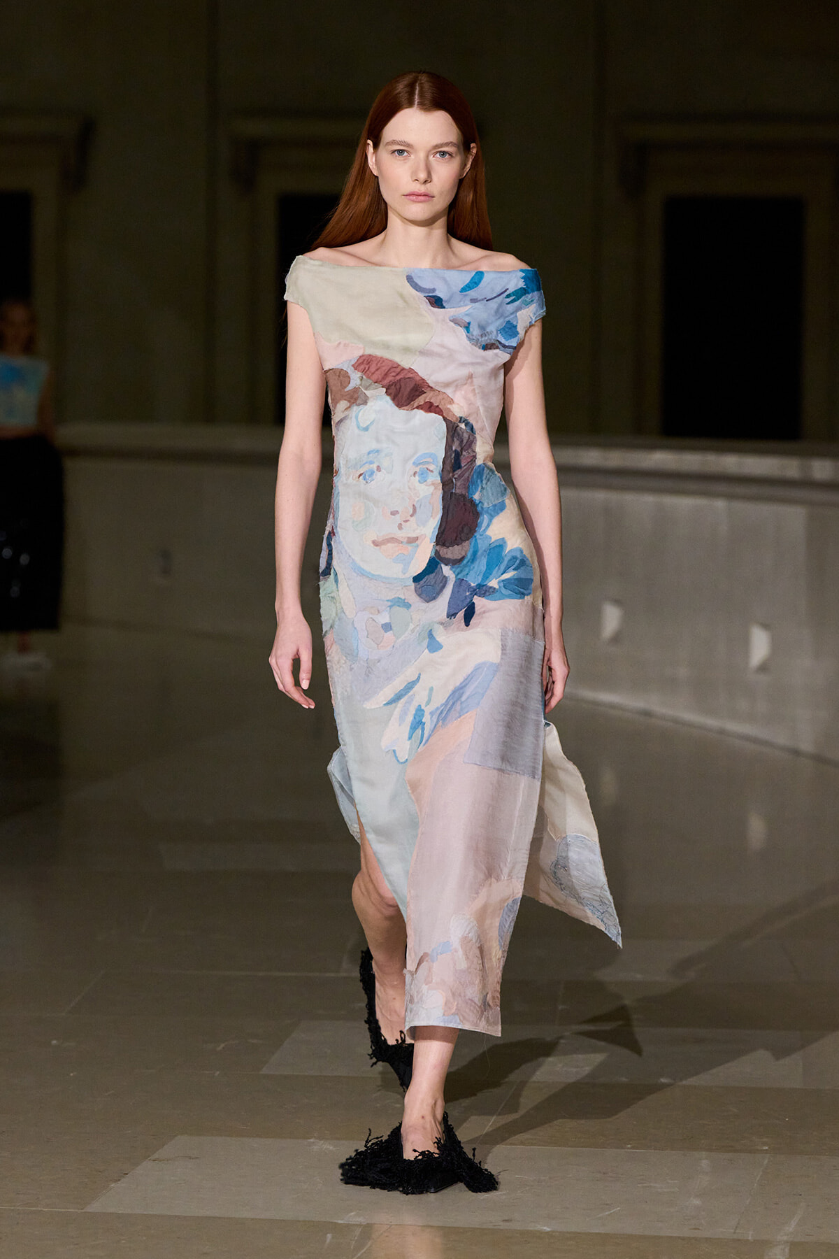 Model walking a runway in a pastel off-the-shoulder dress with an abstract print and flowing skirt.