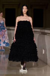 Model walking the runway in a strapless black textured gown with a voluminous skirt, dark hair, and a neutral expression.