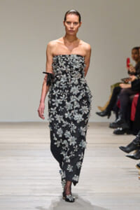 Strapless black gown covered in silver floral appliqués walking the runway, model with sleek hair and a focused expression.
