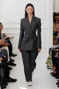 Female model walks a fashion runway in a oversized double-breasted gray suit, white sneakers