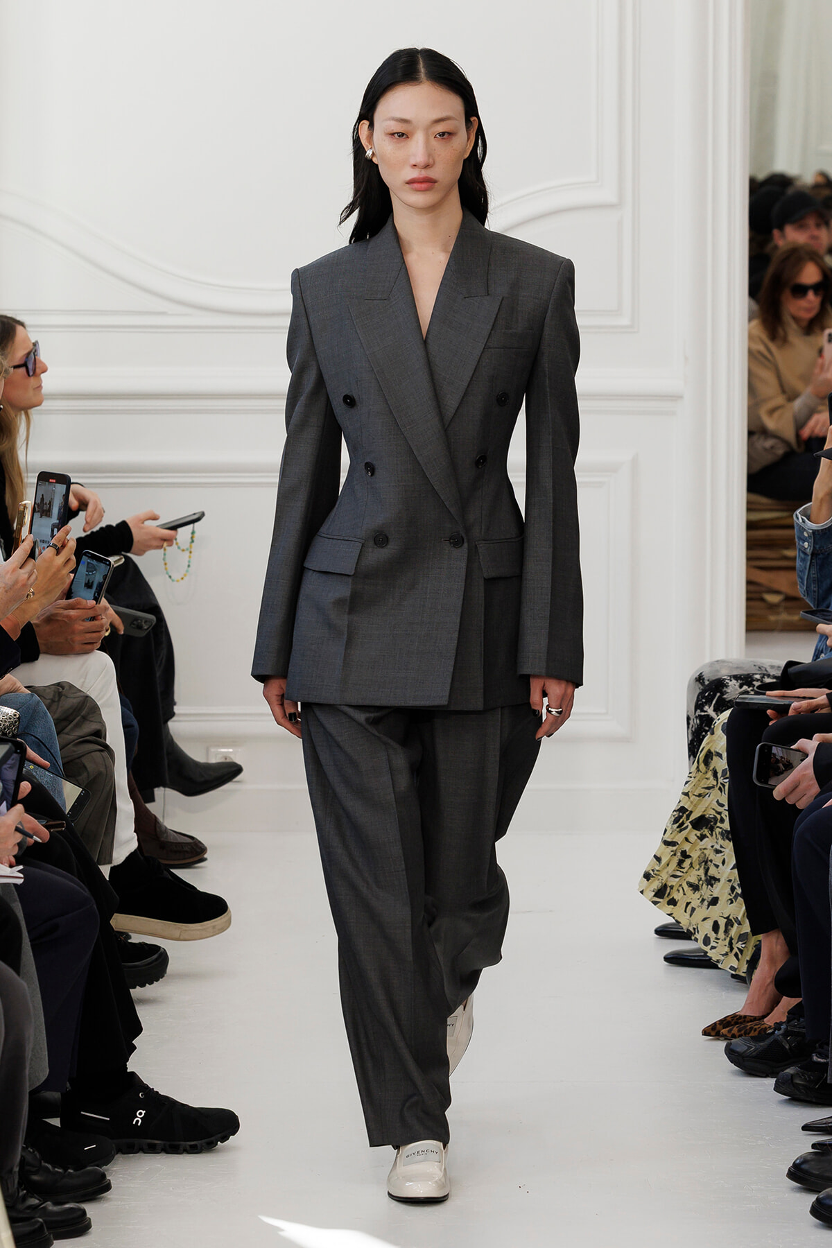 Female model walks a fashion runway in a oversized double-breasted gray suit, white sneakers