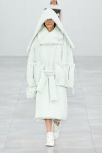 Model walking a runway in a voluminous pale mint-green hooded puffer coat with a belt and oversized pockets.