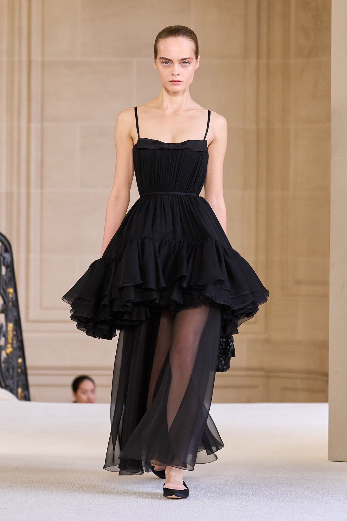 Model walks the runway in a black spaghetti-strap dress with a tiered, ruffled skirt.