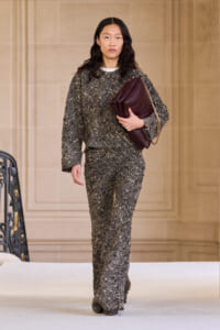 Model on a runway wearing a glittery gray tweed suit and carrying a burgundy clutch.