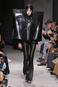 Model walks the runway in an oversized black leather angular jacket and snakeskin pants.