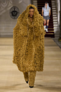 Model walking the runway in a full-length brown shaggy fur outfit with a hood and matching pants, filling the look from head to toe.