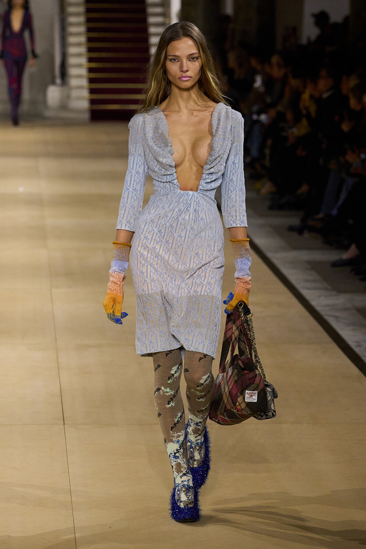 Model walks the runway in a light-blue patterned dress with a plunging neckline, gloves, printed tights, blue glitter boots, and a plaid handbag.