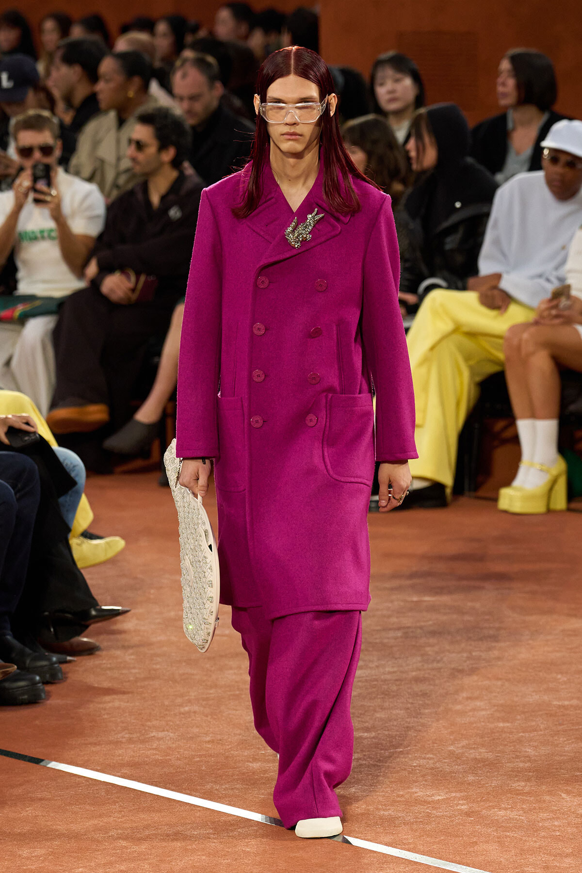 Model walking the runway in a bright magenta double-breasted coat with large front pockets and a decorative brooch.
