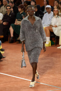 Model walks the runway in a silver glittery textured two-piece outfit with oversized sunglasses and a metallic handbag.