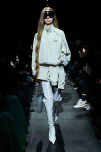 Runway model in a pale mint oversized jacket with matching shorts, tall white thigh-high boots, and a large black visor.