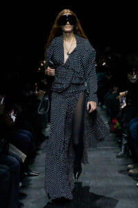 Model walks runway in a navy polka-dot matching set with a deep V neckline, sheer panel, and oversized black sunglasses.