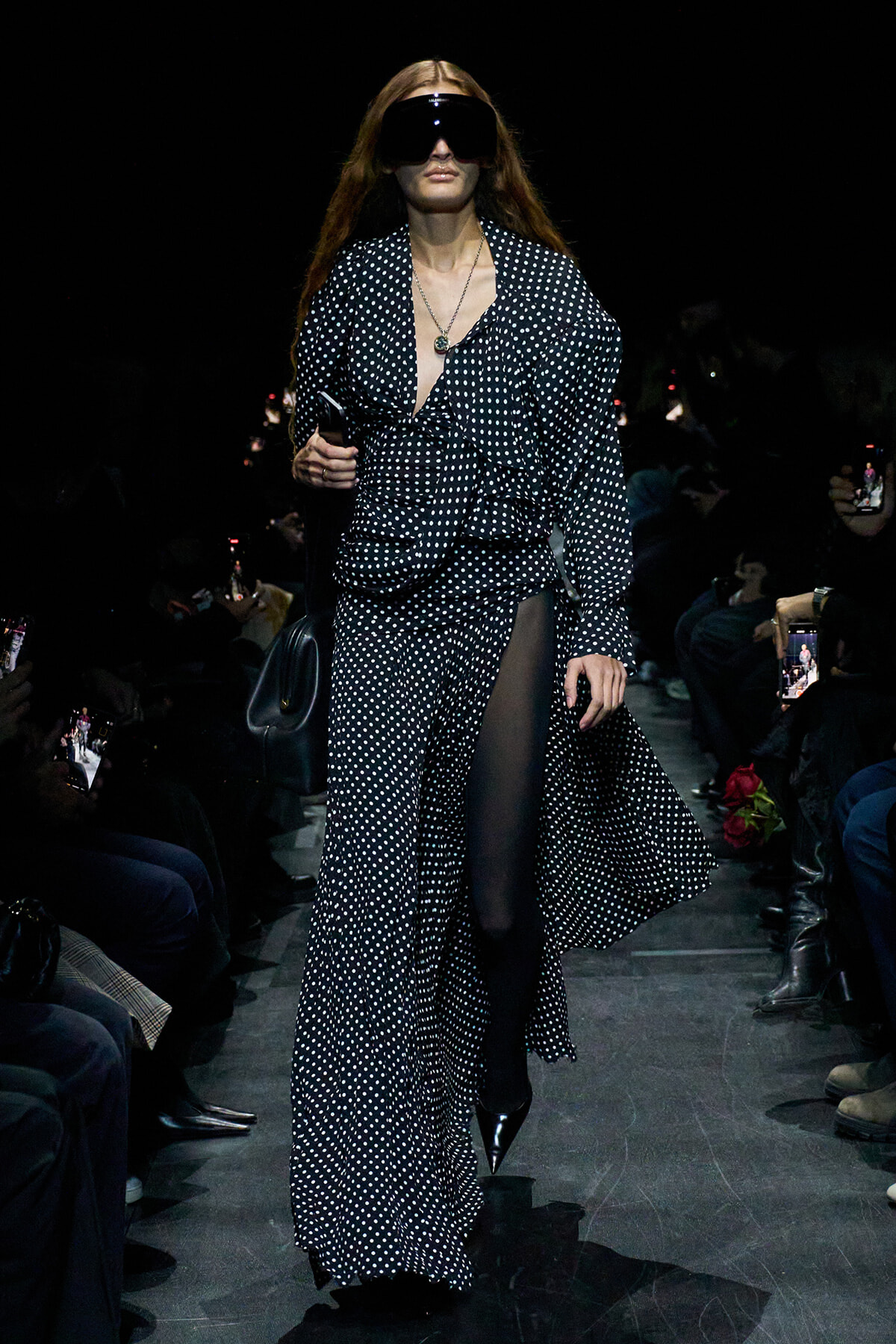 Model walks runway in a navy polka-dot matching set with a deep V neckline, sheer panel, and oversized black sunglasses.