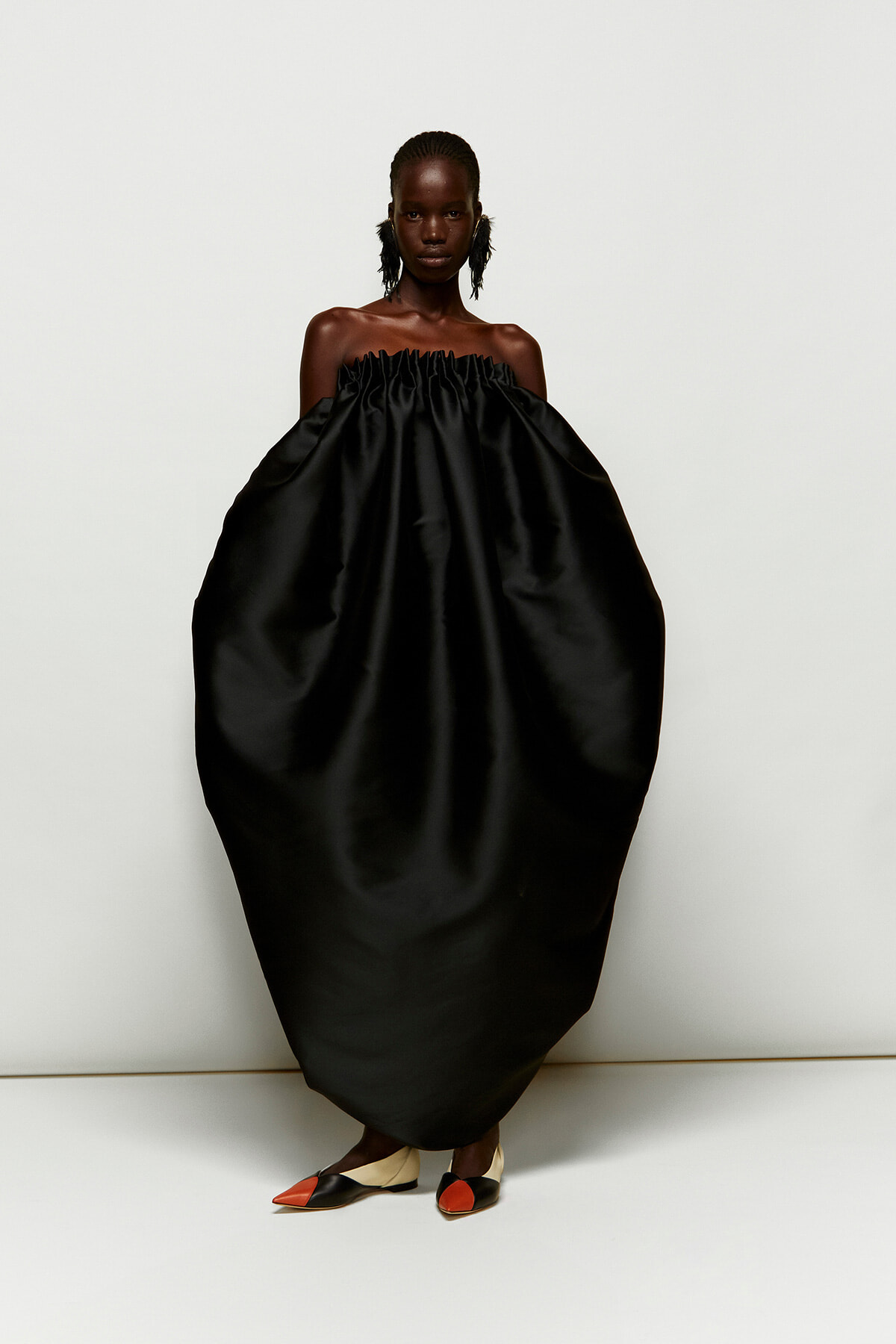 Model wearing an oversized off-shoulder black gown with smocked top, standing against a light background.