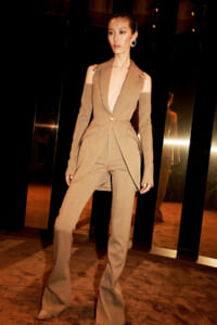 Asian female model in a beige tailored suit with shoulder-cutouts, walking a fashion runway.