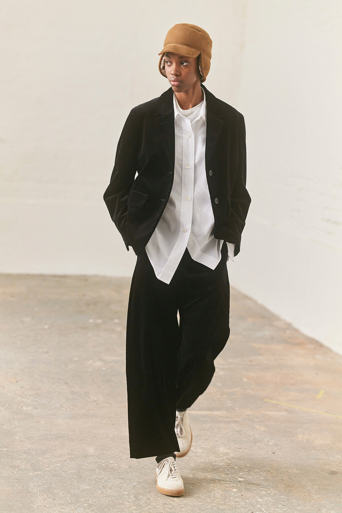 Person wearing a black velvet blazer and wide-leg trousers with a white button-up shirt, tan bucket hat, and white sneakers indoors.