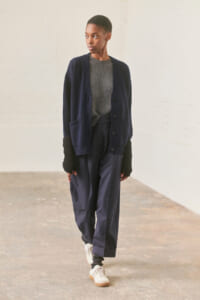 Model wearing a navy cardigan over a gray knit sweater with wide‑leg navy trousers and white sneakers, standing in a minimalist studio setting.