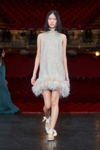Model walks the runway in a sleeveless silver bead-dotted dress with a fluffy white feather hem.
