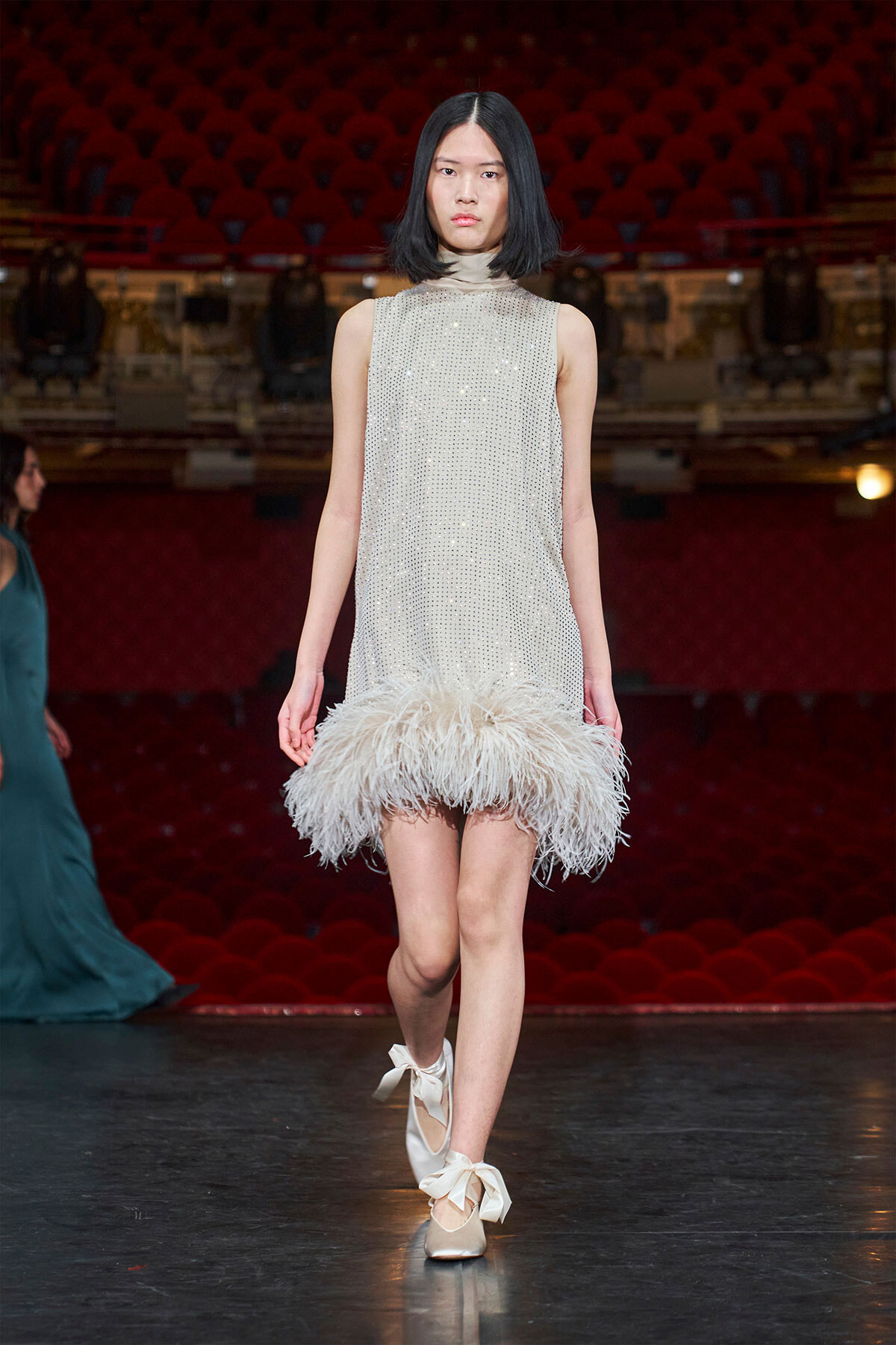 Model walks the runway in a sleeveless silver bead-dotted dress with a fluffy white feather hem.