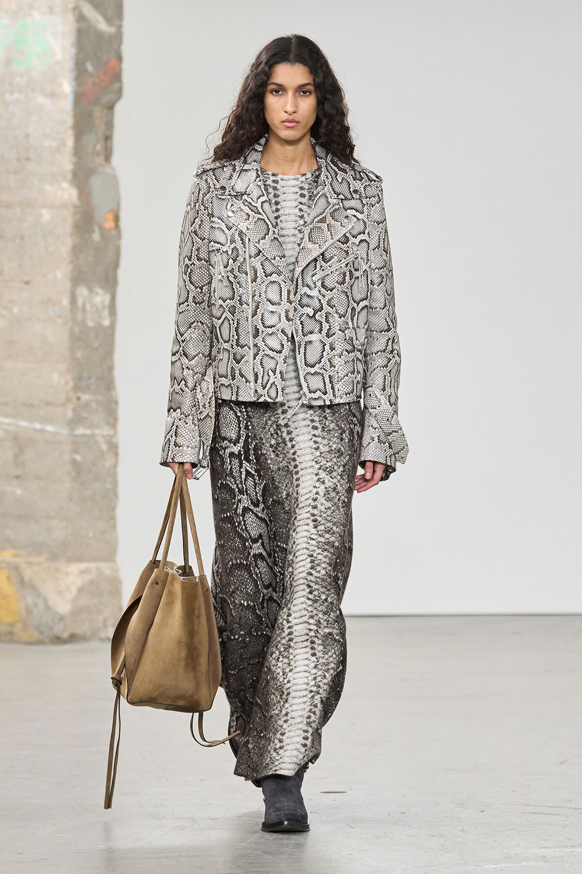 Model walks the runway in a gray snakeskin-print blazer and matching long skirt, carrying a tan suede tote.
