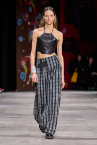 Model walks runway in a black leather halter crop top with studded neckline and loose plaid wide-leg pants.