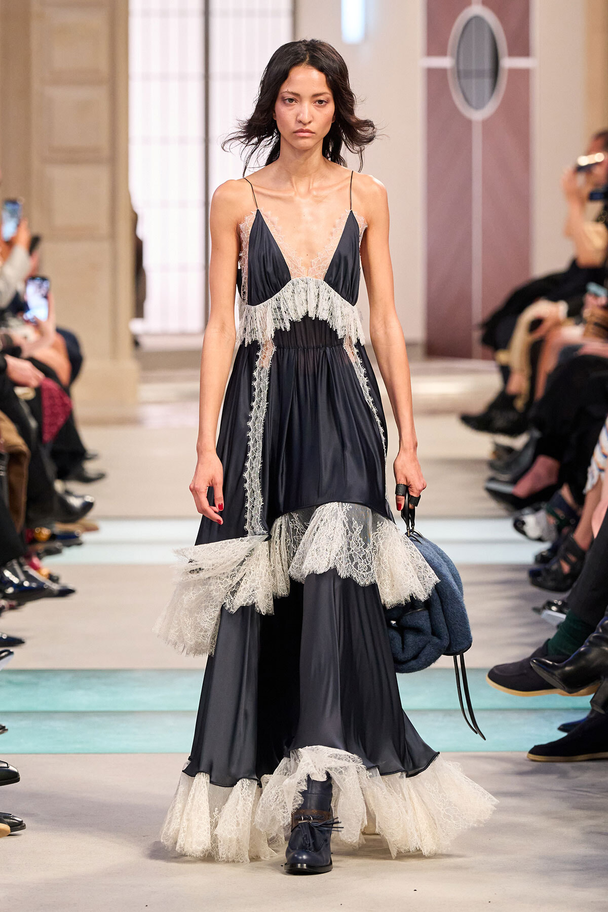 Model walks the runway in a navy slip dress with sheer lace panels and layered lace-trimmed skirt.