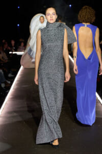 Model walks the runway in a gray leopard-print sleeveless gown with a high neckline and a draped cape detail over one shoulder.