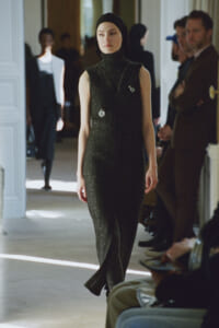 Model walks down a runway wearing a sleeveless glittery black turtleneck jumpsuit and hijab.