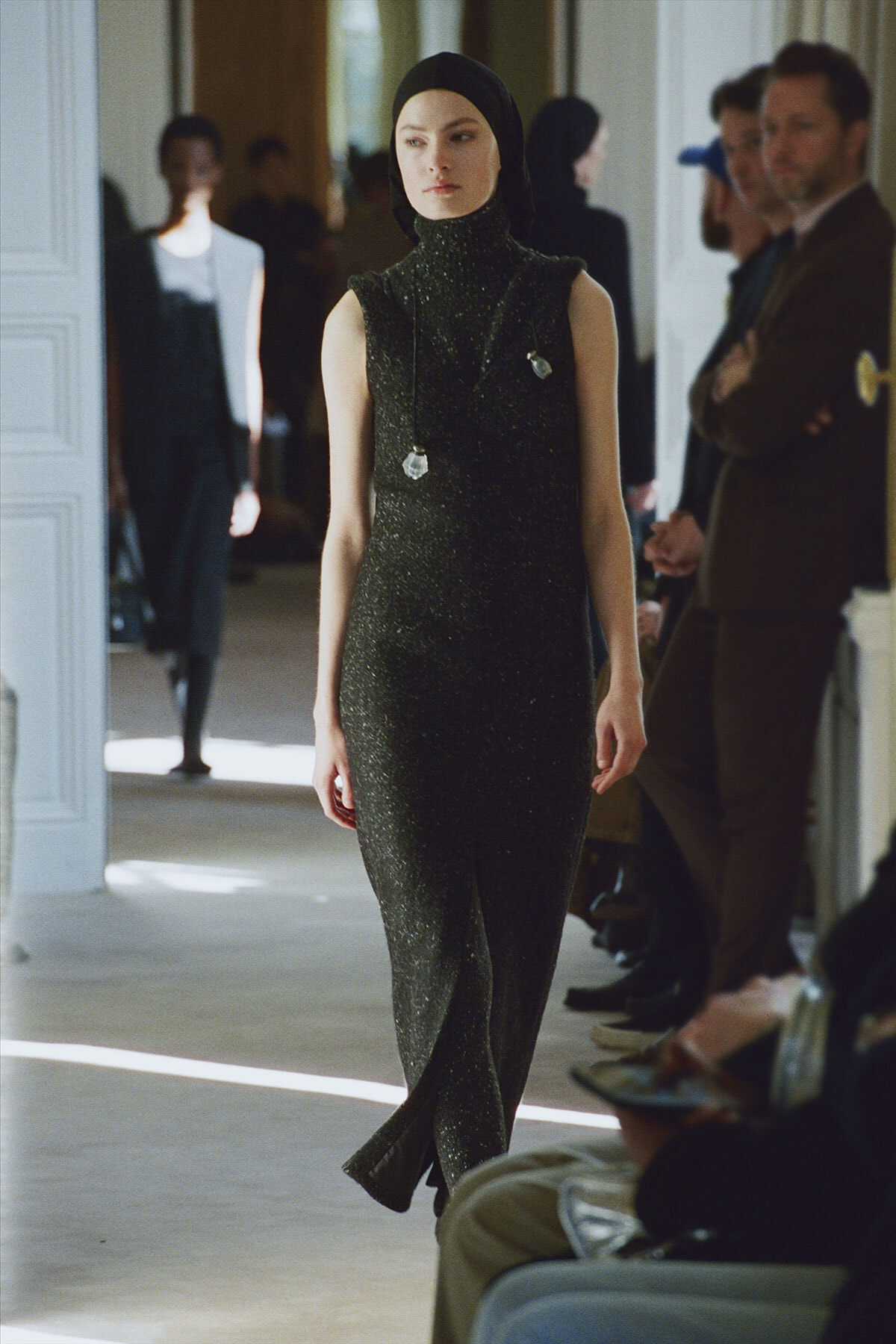 Model walks down a runway wearing a sleeveless glittery black turtleneck jumpsuit and hijab.