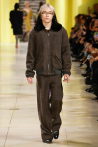 Model walks the runway in a brown fleece zip-up jacket with matching wide-leg pants; black fur collar and glossy black shoes.